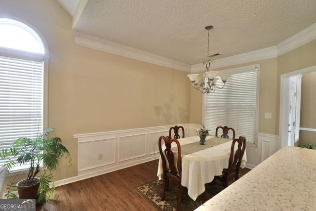 dining room with ornamental molding, a textured ceiling, dark wood-type flooring, and a notable chandelier