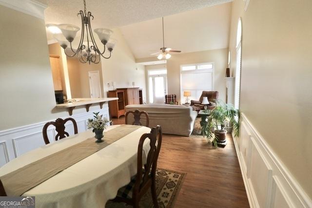 dining room with a textured ceiling, ceiling fan with notable chandelier, dark wood-type flooring, and vaulted ceiling