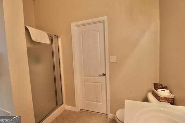 bathroom with tile patterned flooring, a shower with shower door, and toilet