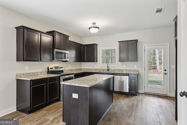 kitchen with hardwood / wood-style floors, a kitchen island, sink, and appliances with stainless steel finishes