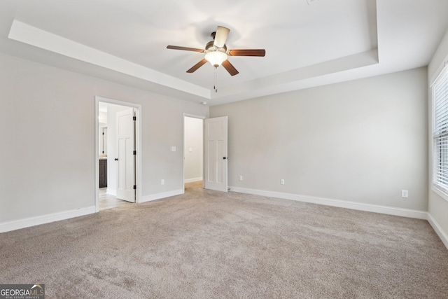 empty room with a tray ceiling, ceiling fan, and light colored carpet