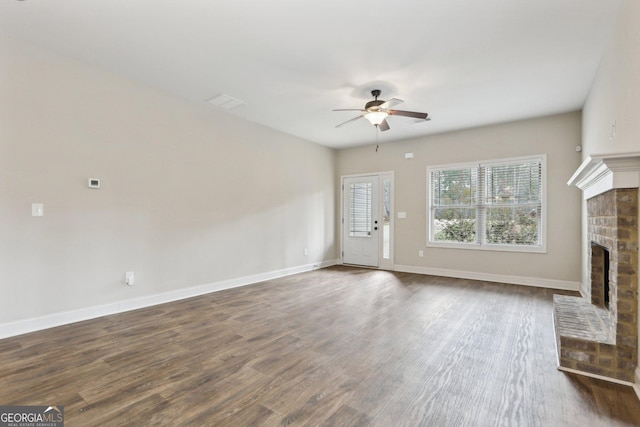 unfurnished living room featuring ceiling fan, dark wood-type flooring, and a brick fireplace