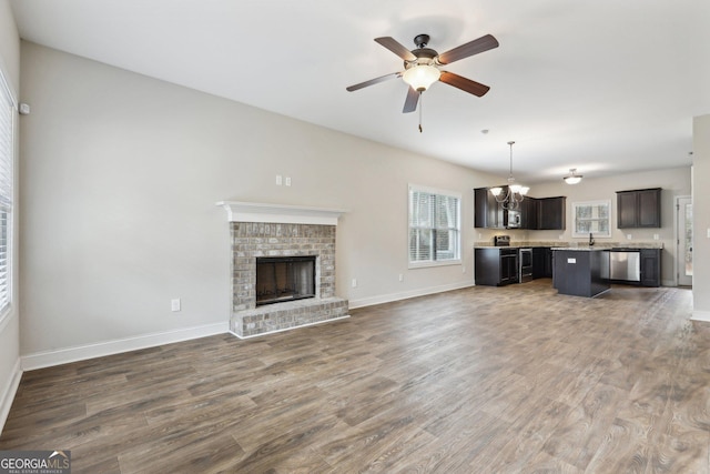 unfurnished living room featuring ceiling fan with notable chandelier, dark hardwood / wood-style floors, a brick fireplace, and sink