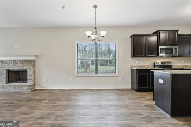 kitchen with hardwood / wood-style flooring, a fireplace, decorative light fixtures, stainless steel appliances, and a chandelier