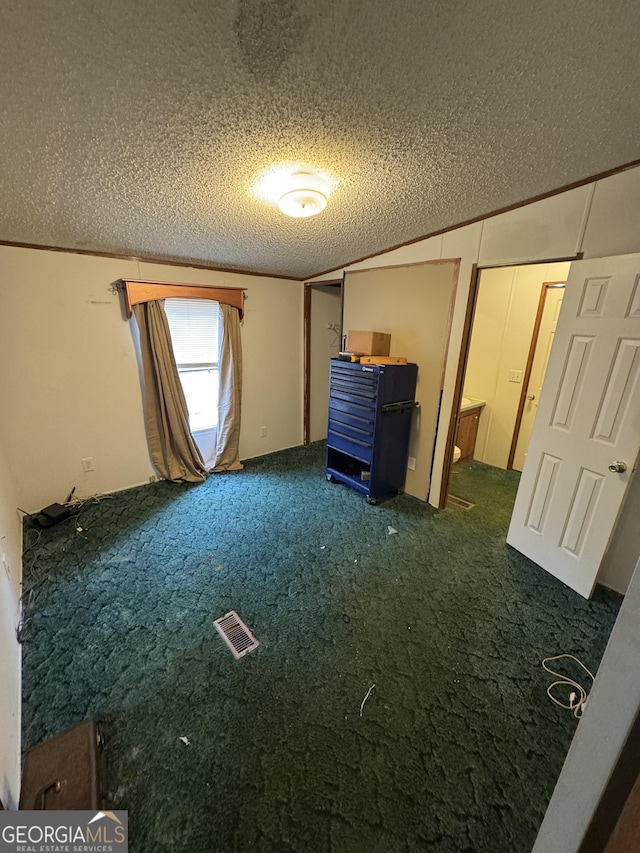 unfurnished bedroom featuring dark colored carpet, ensuite bathroom, crown molding, vaulted ceiling, and a textured ceiling