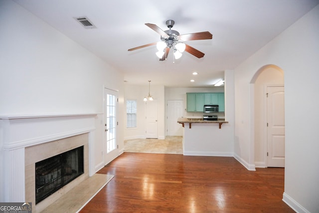 unfurnished living room featuring a fireplace, ceiling fan with notable chandelier, and hardwood / wood-style flooring