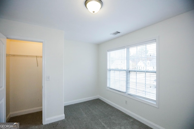 unfurnished bedroom featuring dark colored carpet, a walk in closet, and a closet