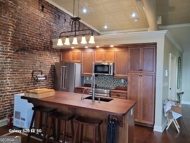 kitchen with sink, dark wood-type flooring, brick wall, pendant lighting, and appliances with stainless steel finishes