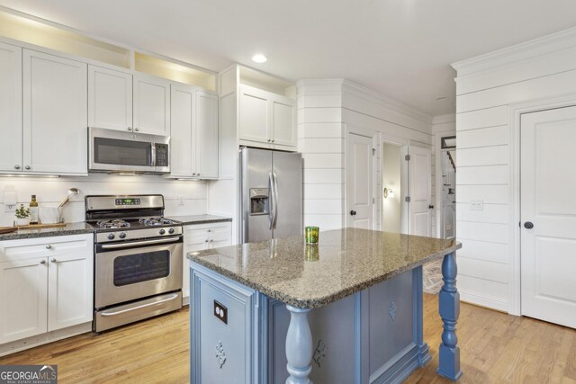 kitchen featuring an inviting chandelier, dark stone countertops, light wood-type flooring, a kitchen island, and ornamental molding