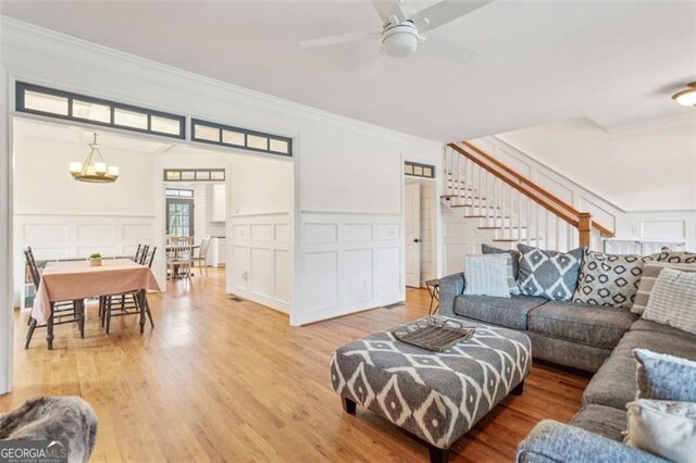 living room with built in features, light hardwood / wood-style flooring, ceiling fan, and ornamental molding