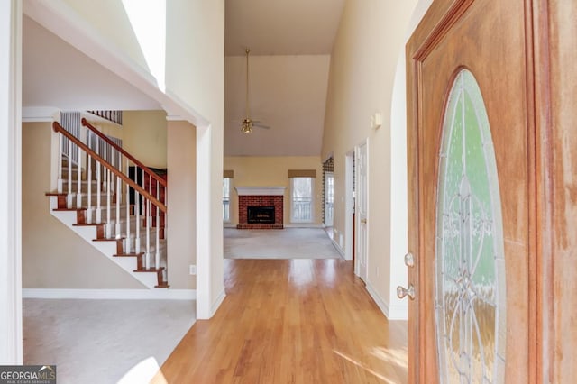 entrance foyer featuring ceiling fan, a towering ceiling, light wood-type flooring, and a brick fireplace