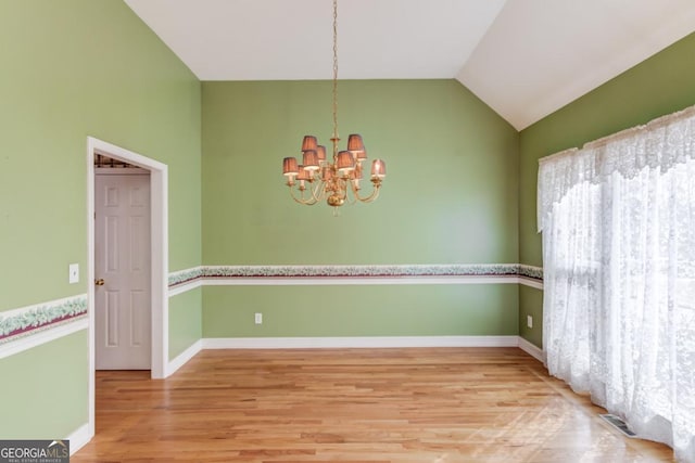 unfurnished room with hardwood / wood-style floors, lofted ceiling, and an inviting chandelier