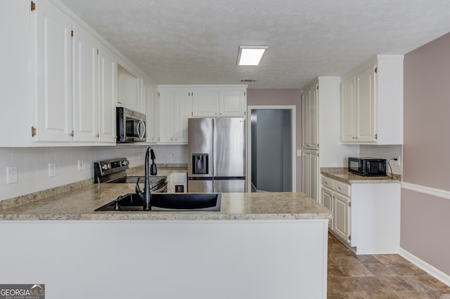 kitchen with kitchen peninsula, white cabinetry, sink, and appliances with stainless steel finishes