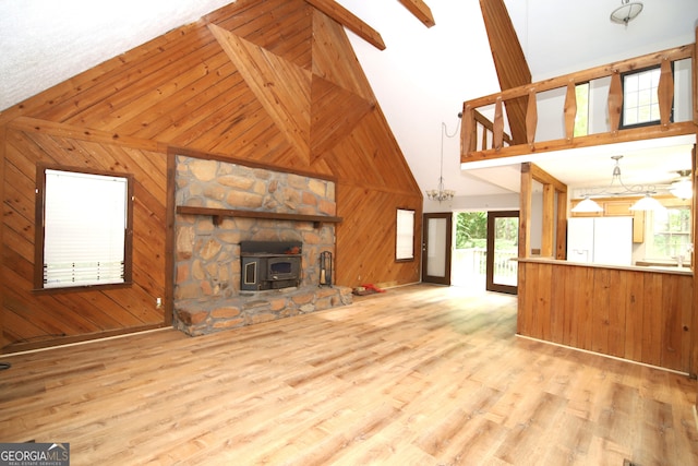 unfurnished living room featuring high vaulted ceiling, beam ceiling, a wood stove, and wooden walls