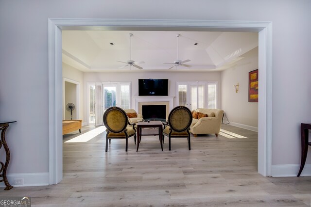 sitting room with ceiling fan, a raised ceiling, and light wood-type flooring