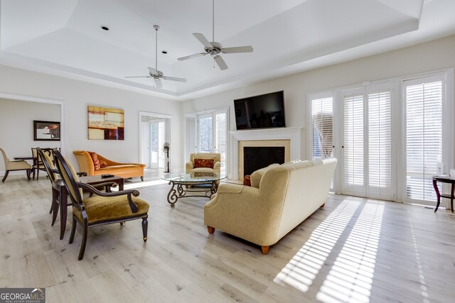 living room with a tray ceiling, a wealth of natural light, ceiling fan, and light wood-type flooring