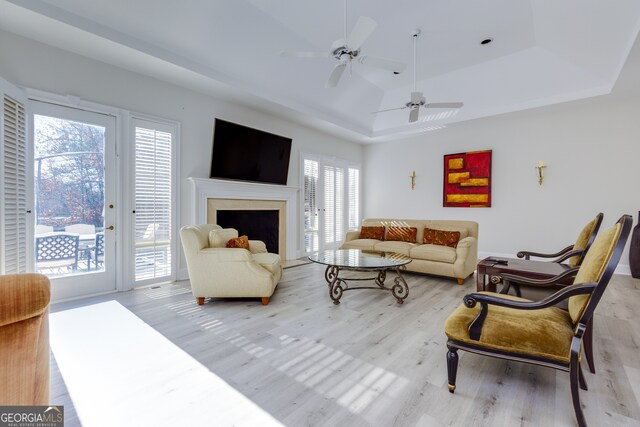 living room featuring plenty of natural light, ceiling fan, a raised ceiling, and light wood-type flooring