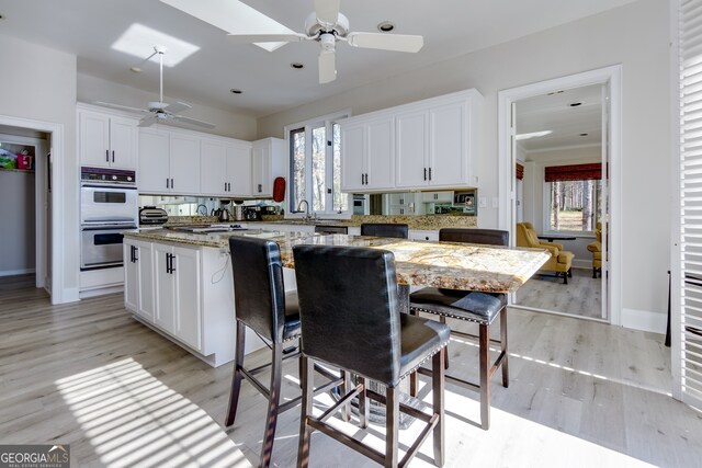 kitchen featuring a skylight, a kitchen island, white cabinets, light stone counters, and double wall oven