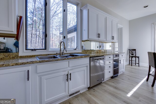 kitchen featuring dishwasher, sink, light hardwood / wood-style floors, dark stone counters, and white cabinets