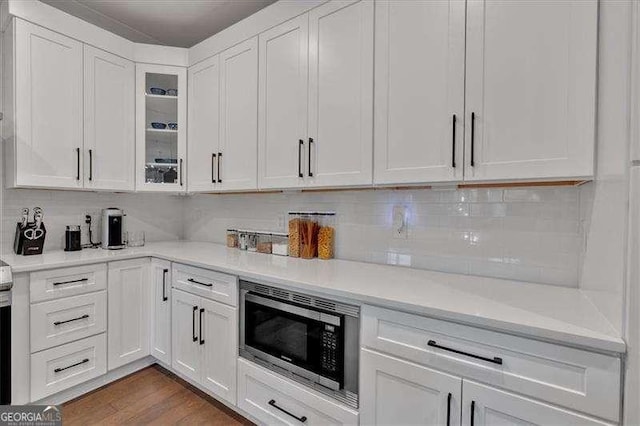 kitchen featuring white cabinetry, stainless steel microwave, decorative backsplash, and light countertops