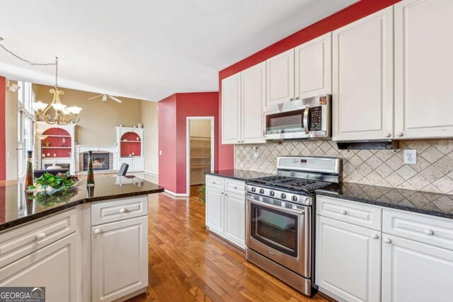 kitchen featuring stainless steel appliances, tasteful backsplash, dark stone counters, decorative light fixtures, and white cabinets