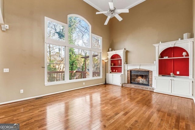 unfurnished living room featuring ceiling fan, a healthy amount of sunlight, a brick fireplace, wood-type flooring, and ornamental molding