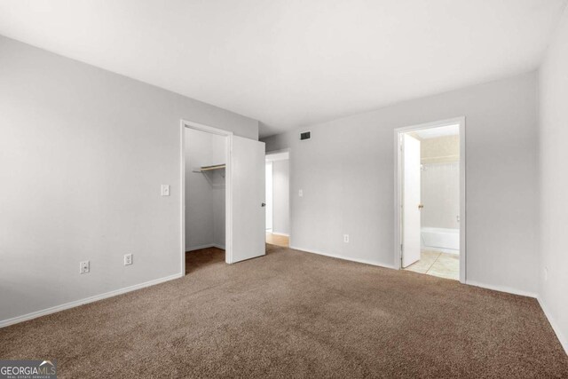 unfurnished bedroom with light carpet, a walk in closet, ensuite bath, and a closet