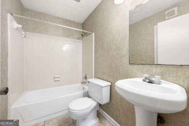 bathroom featuring tile patterned flooring, a textured ceiling, toilet, and tiled shower / bath