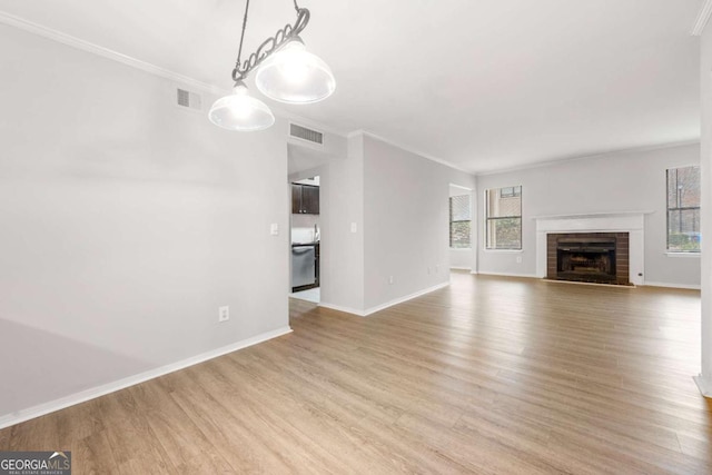 unfurnished living room with light hardwood / wood-style floors, crown molding, a fireplace, and a wealth of natural light