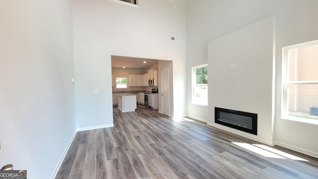 unfurnished living room with light wood-type flooring and a towering ceiling