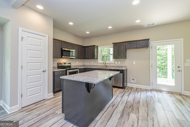 kitchen featuring dark brown cabinetry, a kitchen bar, light hardwood / wood-style flooring, a kitchen island, and stainless steel appliances