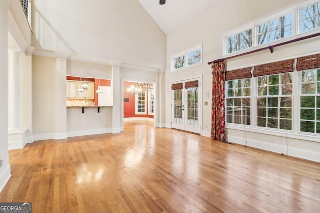 unfurnished living room featuring french doors, high vaulted ceiling, a chandelier, and light hardwood / wood-style floors