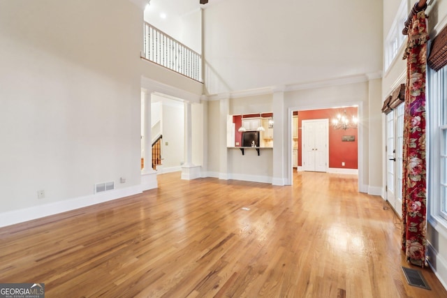 unfurnished living room featuring light hardwood / wood-style flooring, a high ceiling, and an inviting chandelier