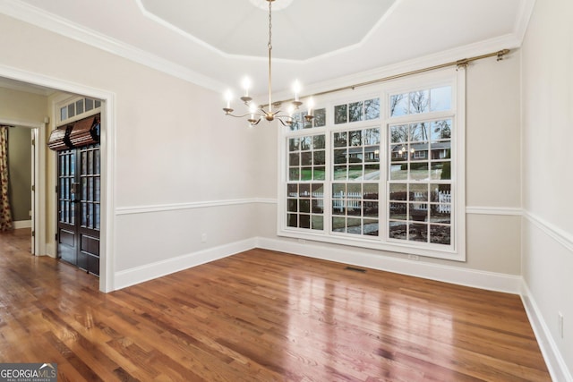 unfurnished dining area with hardwood / wood-style flooring, a notable chandelier, ornamental molding, and a tray ceiling