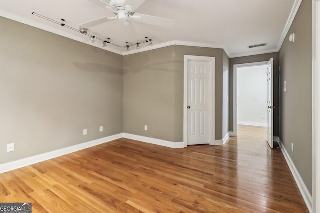 empty room featuring wood-type flooring, track lighting, ceiling fan, and ornamental molding