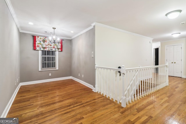 empty room with a chandelier, hardwood / wood-style floors, and ornamental molding