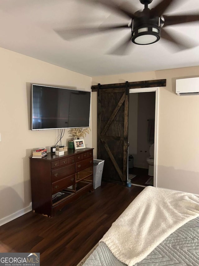 bedroom featuring a wall mounted air conditioner, ceiling fan, dark wood-type flooring, a barn door, and connected bathroom