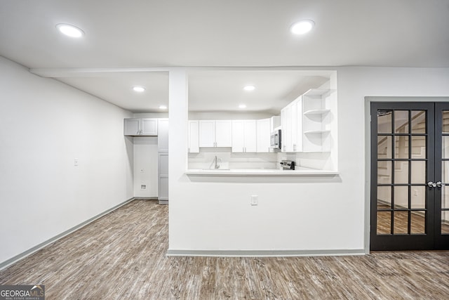 kitchen featuring hardwood / wood-style floors, kitchen peninsula, sink, white cabinets, and french doors