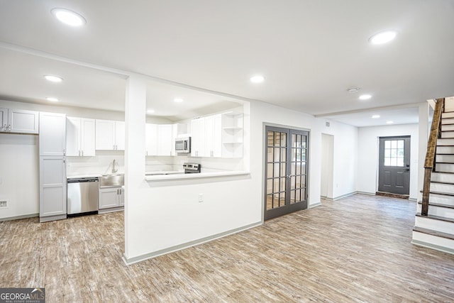 kitchen featuring light hardwood / wood-style floors, kitchen peninsula, appliances with stainless steel finishes, white cabinets, and sink