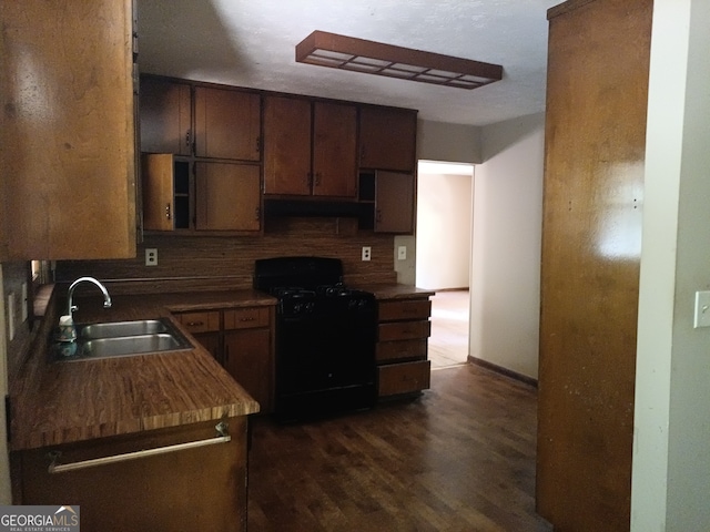 kitchen featuring dark hardwood / wood-style flooring, backsplash, black range oven, dark brown cabinetry, and sink