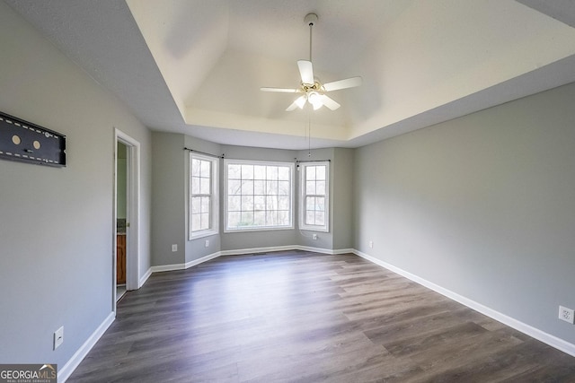 empty room featuring ceiling fan, dark hardwood / wood-style flooring, and a tray ceiling