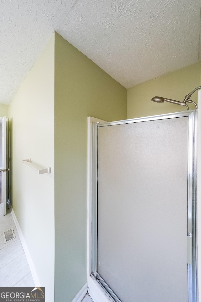 bathroom featuring a textured ceiling, tile patterned floors, and an enclosed shower