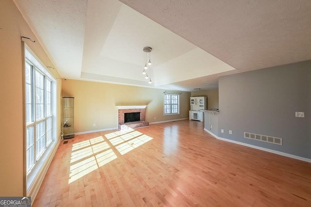 unfurnished living room with a brick fireplace, plenty of natural light, light hardwood / wood-style floors, and a tray ceiling