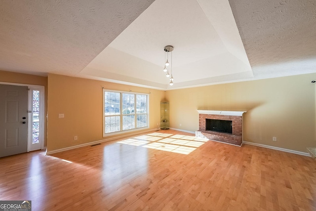 unfurnished living room featuring a fireplace, a tray ceiling, and light hardwood / wood-style flooring