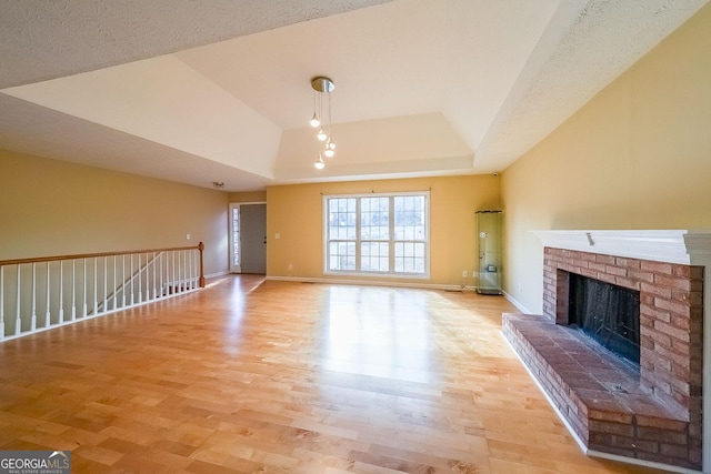 unfurnished living room featuring a tray ceiling, a fireplace, light hardwood / wood-style floors, and a textured ceiling