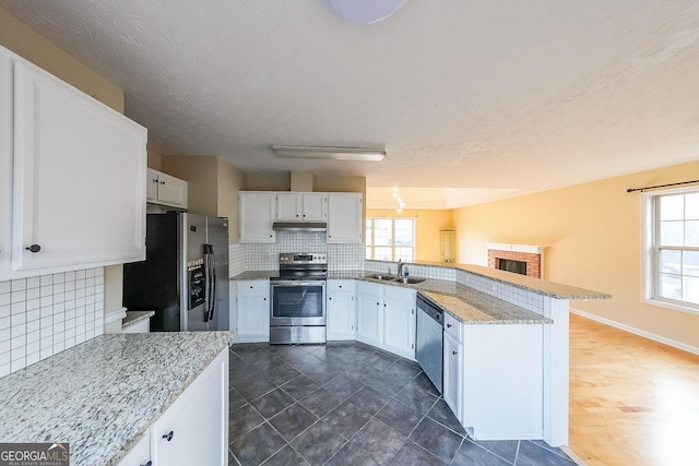 kitchen with white cabinetry, sink, stainless steel appliances, light stone counters, and kitchen peninsula