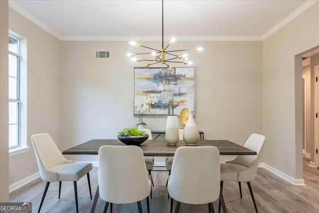 dining space with light hardwood / wood-style floors, crown molding, and an inviting chandelier