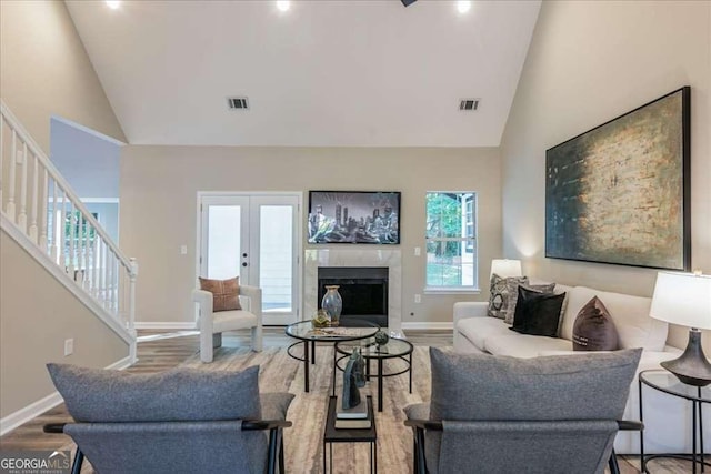 living room featuring a high end fireplace, french doors, hardwood / wood-style flooring, and high vaulted ceiling