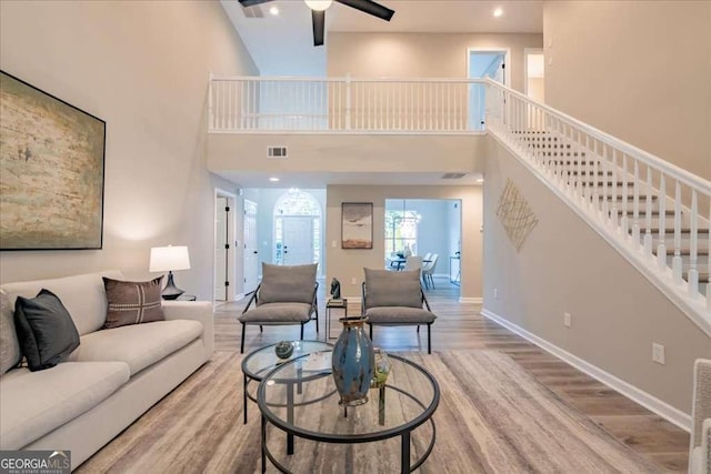 living room with ceiling fan, a towering ceiling, and light hardwood / wood-style floors