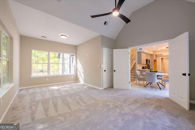 unfurnished living room with ceiling fan, high vaulted ceiling, and light colored carpet